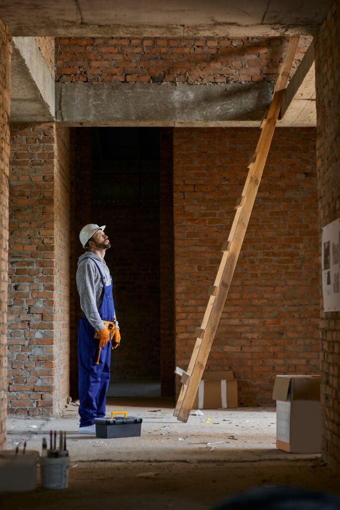 Young workman in blue overalls and hard hat looking up